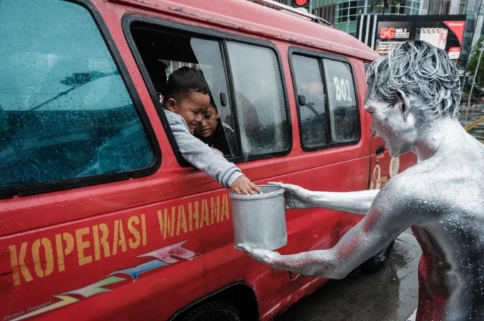 Ari Munandar (phải), với cơ thể được sơn màu bạc, nhận tiền boa tại một ngã tư ở Jakarta.